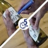 L'image montre des mains écrivant sur des bouteilles de vin à l'aide d'un marqueur, avec un chronomètre affichant 5 minutes.