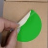 Une main soulève un autocollant vert sur un fond de boîte en carton.