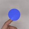 C'est une image d'une main tenant un petit cercle bleu. Le fond est neutre et met en valeur la couleur vive du cercle.