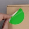 L'image montre une personne qui retire un autocollant vert sur une boîte en carton.